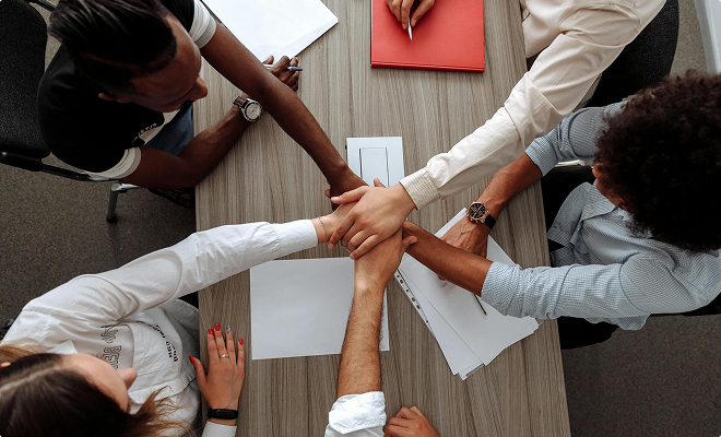 Overhead view of group of people stacking their hands over a desk